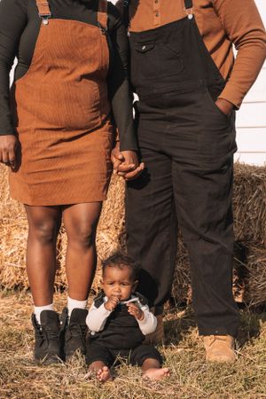 Family wearing coordinating brown overalls posing by hay bales.