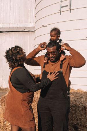 Joyful family moment captured against white barn siding during autumn.
