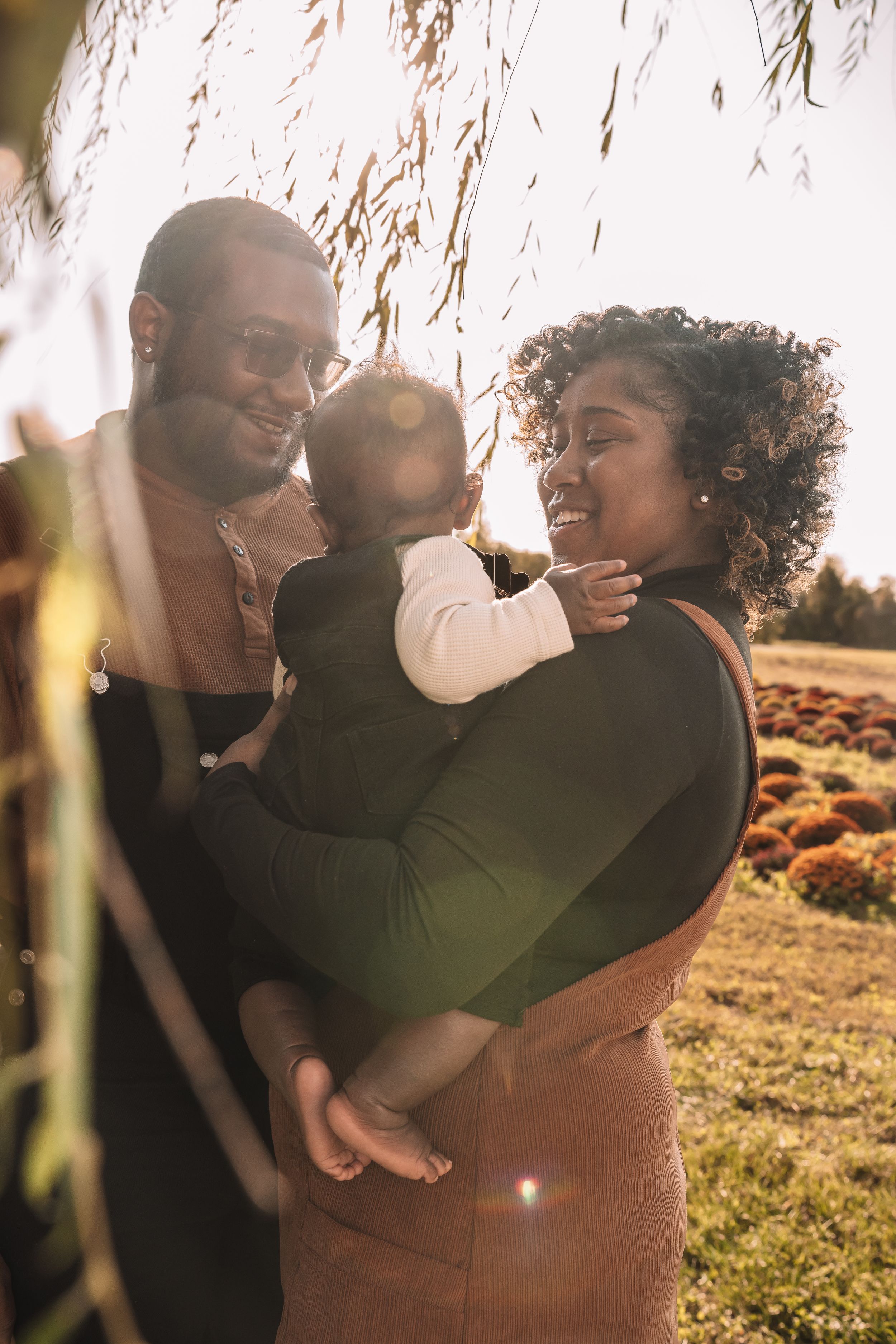 A tender family moment captured in golden sunlight beneath willow branches.