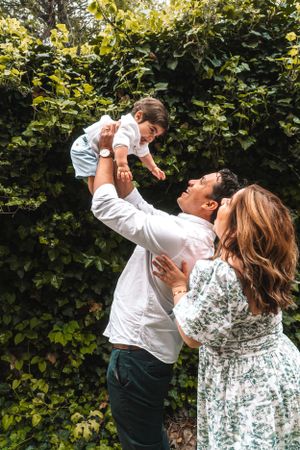 A joyful family moment captured in front of lush green hedges on a sunny day.