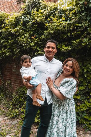 A happy family poses together in front of a vine-covered brick wall.