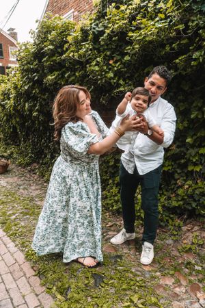 A family shares playful moments together by a vine-covered wall.