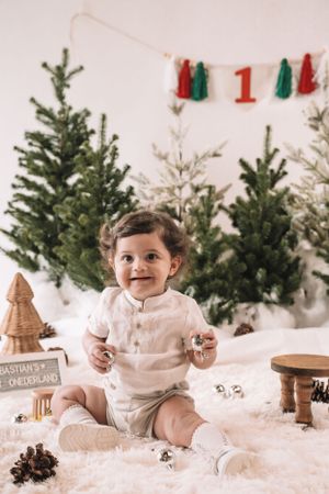 Festive holiday scene with evergreen trees, tassel garland, and decorative wooden ornaments on white fluffy backdrop.