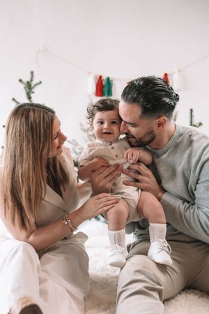 A family shares a tender moment together while sitting on a white fluffy rug with decorative elements in the background.