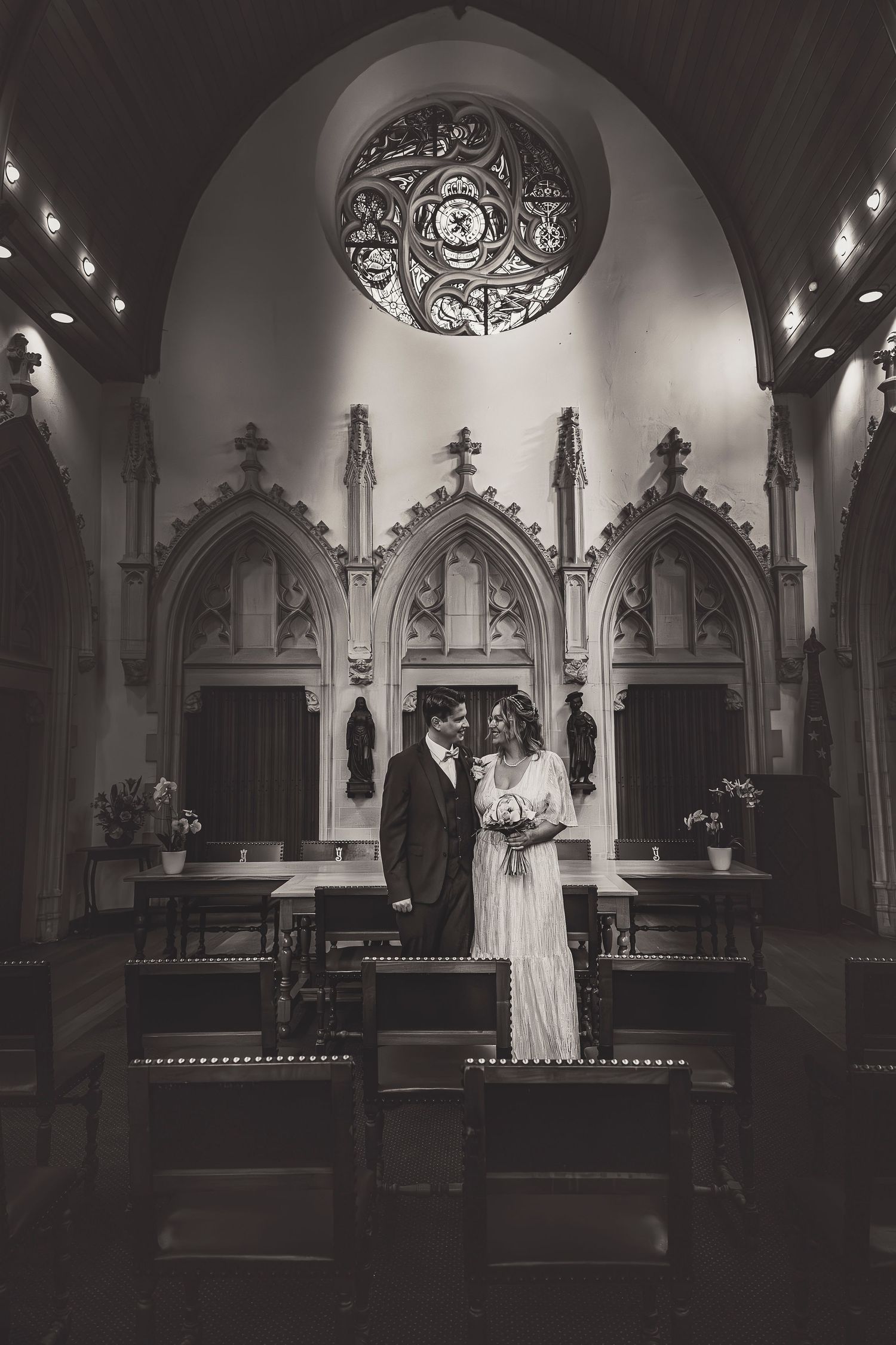 A black and white wedding photo in a Gothic church with ornate arches and a circular stained glass window.