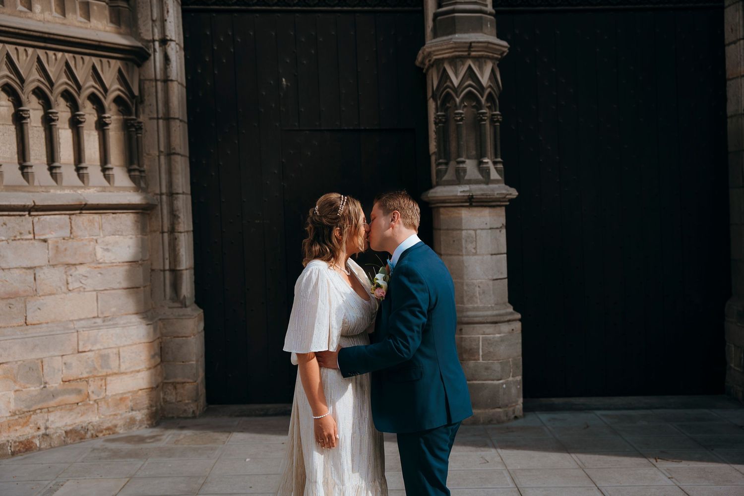 A romantic embrace between newlyweds against gothic stone architecture.