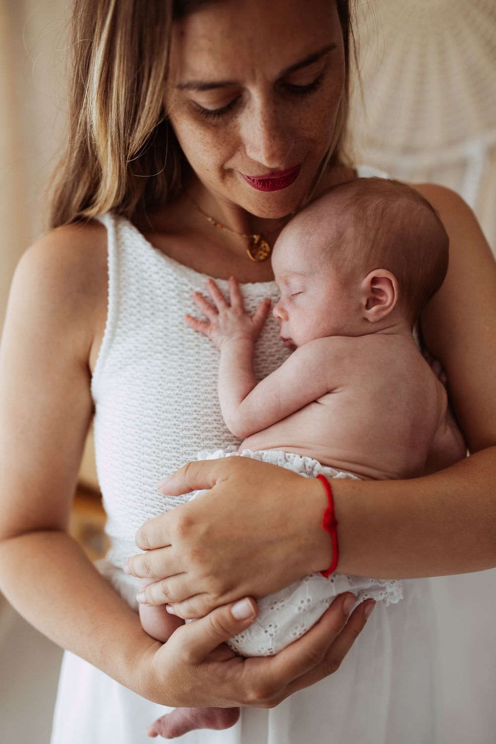 Mother in white dress holding sleeping newborn baby against her chest.