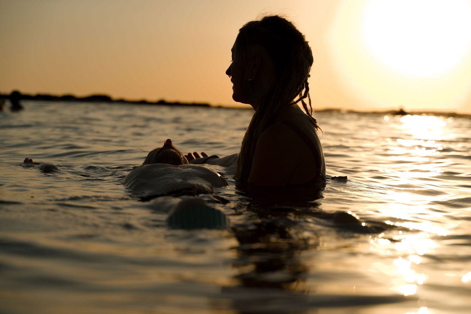 Silhouette of person floating in ocean water during golden sunset.