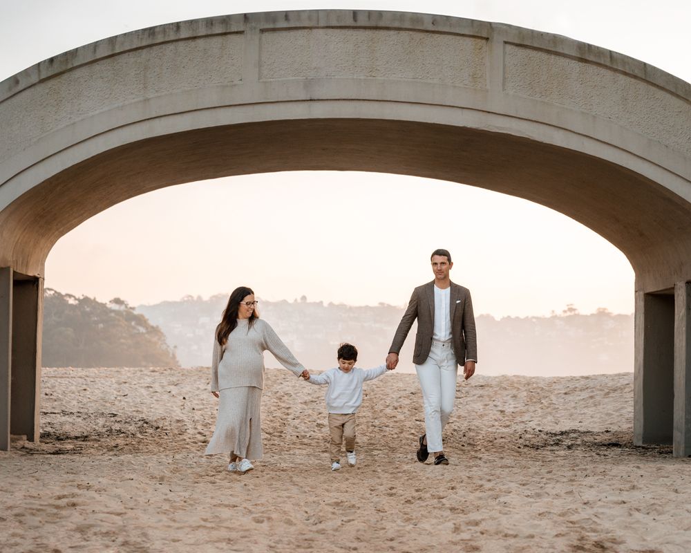 family-of-three-walking-toward-the-camera-under-the-balmoral-beach-bridge-in-mosman