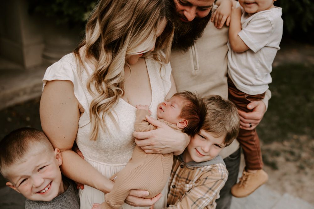 Family of five with newborn baby sharing a tender moment outdoors, surrounded by loving siblings.