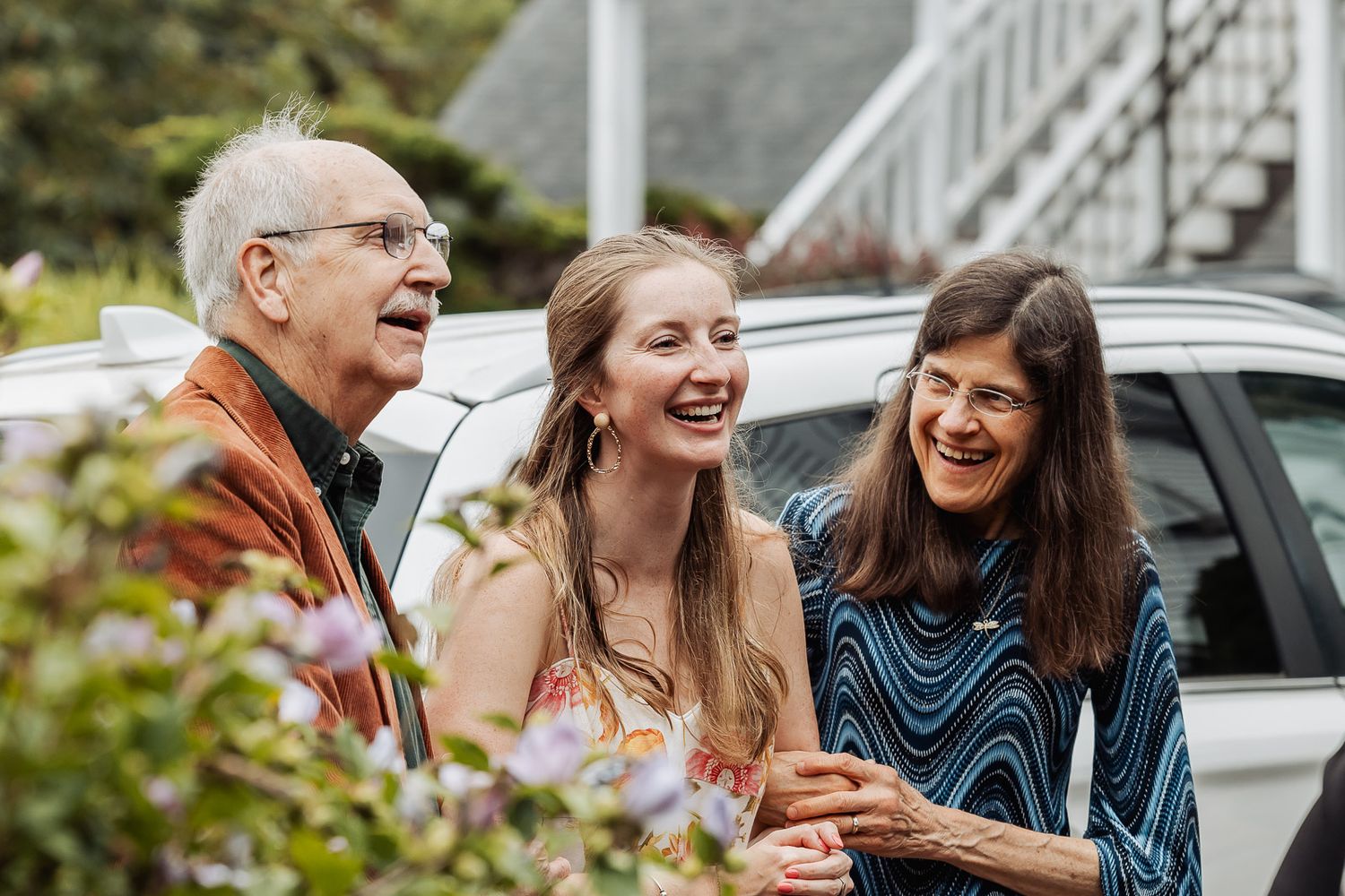 Group sharing joyful laughter outdoors near parked car.