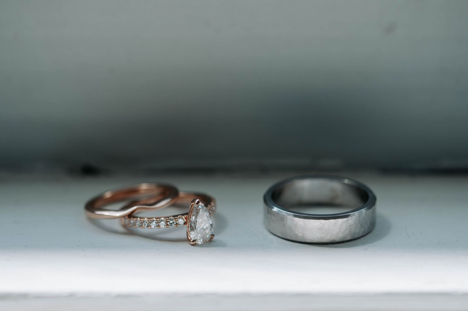 Close-up of diamond engagement ring and plain wedding band on white surface.