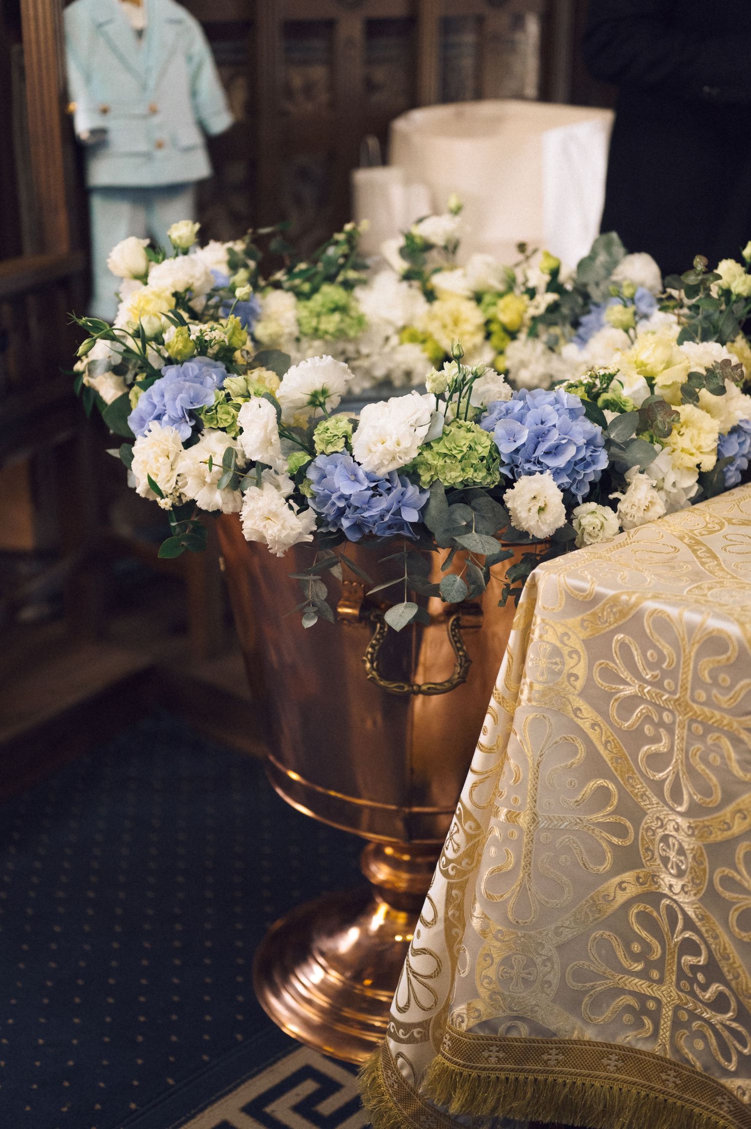 Elegant floral arrangement with blue hydrangeas and white roses adorns a table with delicate lace tablecloth and gold accents.