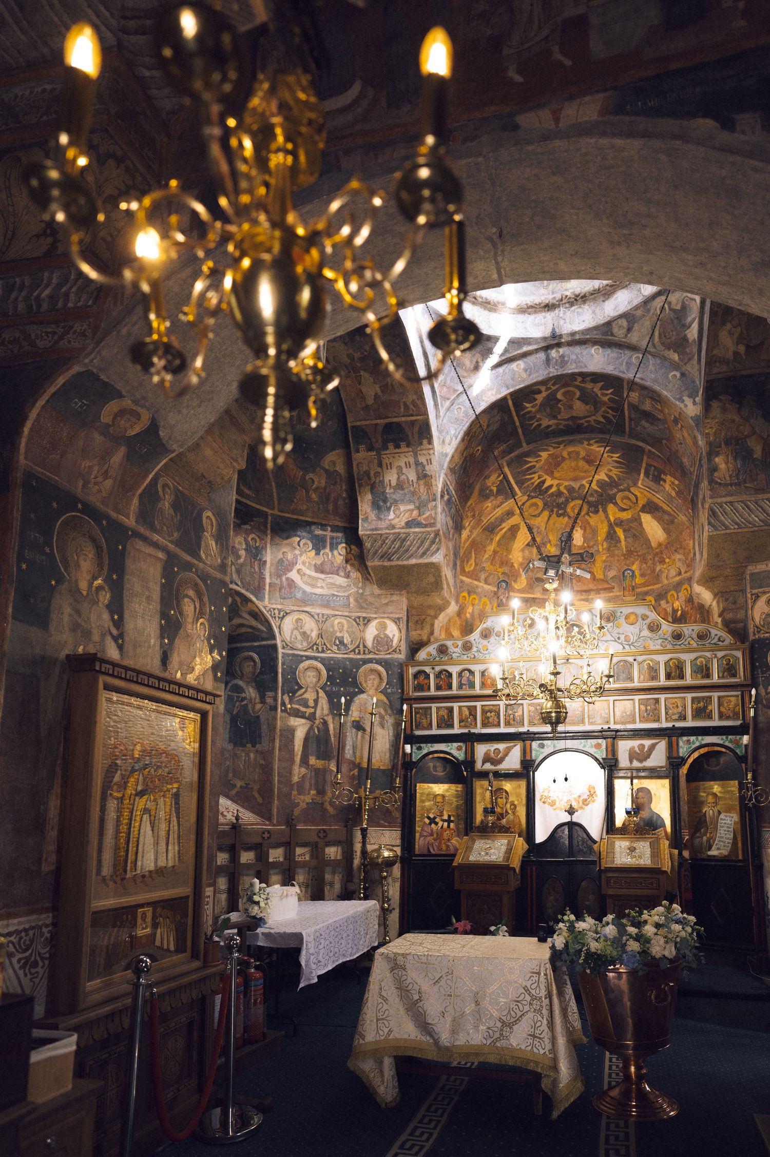 Interior of an ornate Orthodox church with golden chandeliers and detailed frescoes covering the walls and ceiling.
