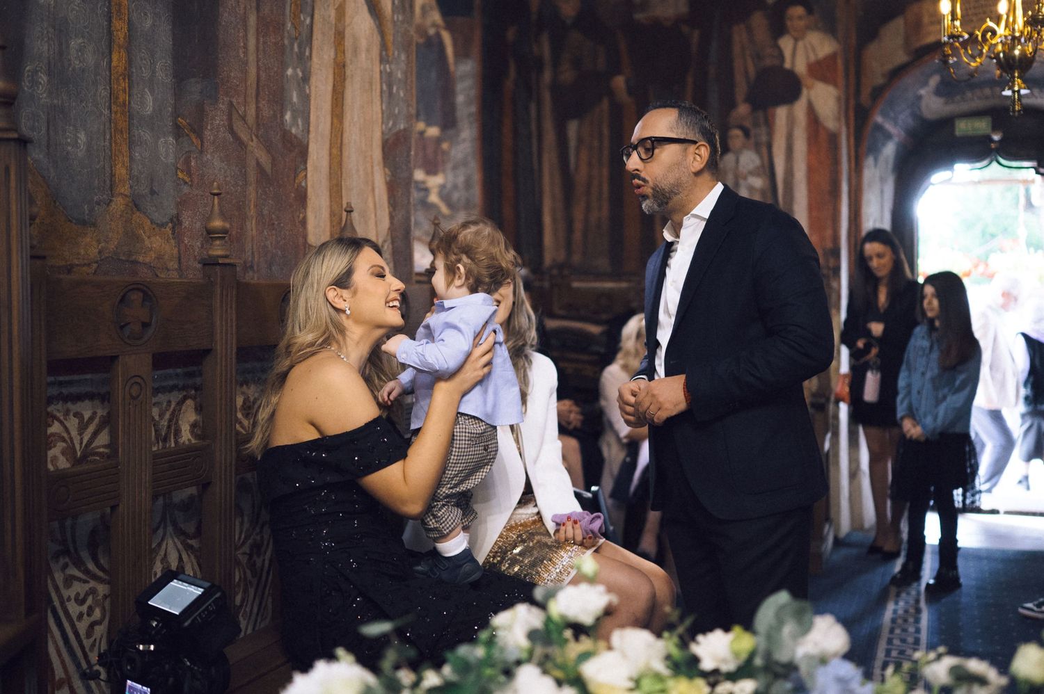 Wedding guests gather in an elegant venue with chandeliers and wooden decor during a reception celebration.
