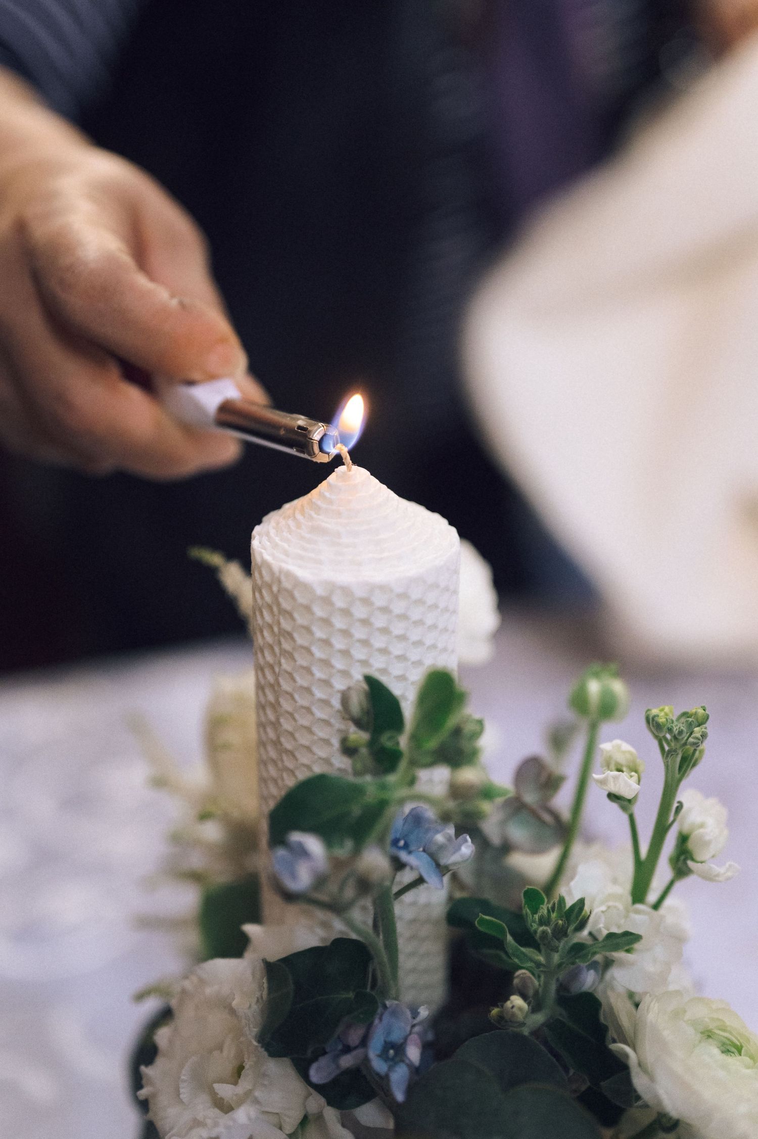 A sequence showing someone lighting a white textured candle surrounded by delicate flowers and greenery.