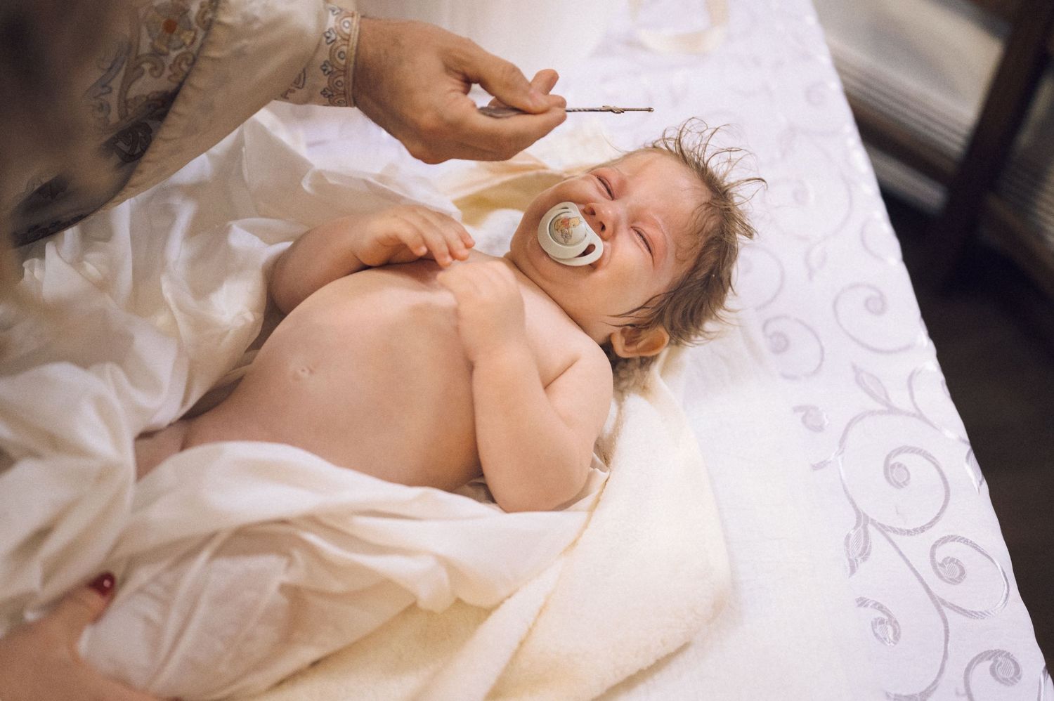 Baby sleeping peacefully in white bedding while holding a pacifier in their mouth.