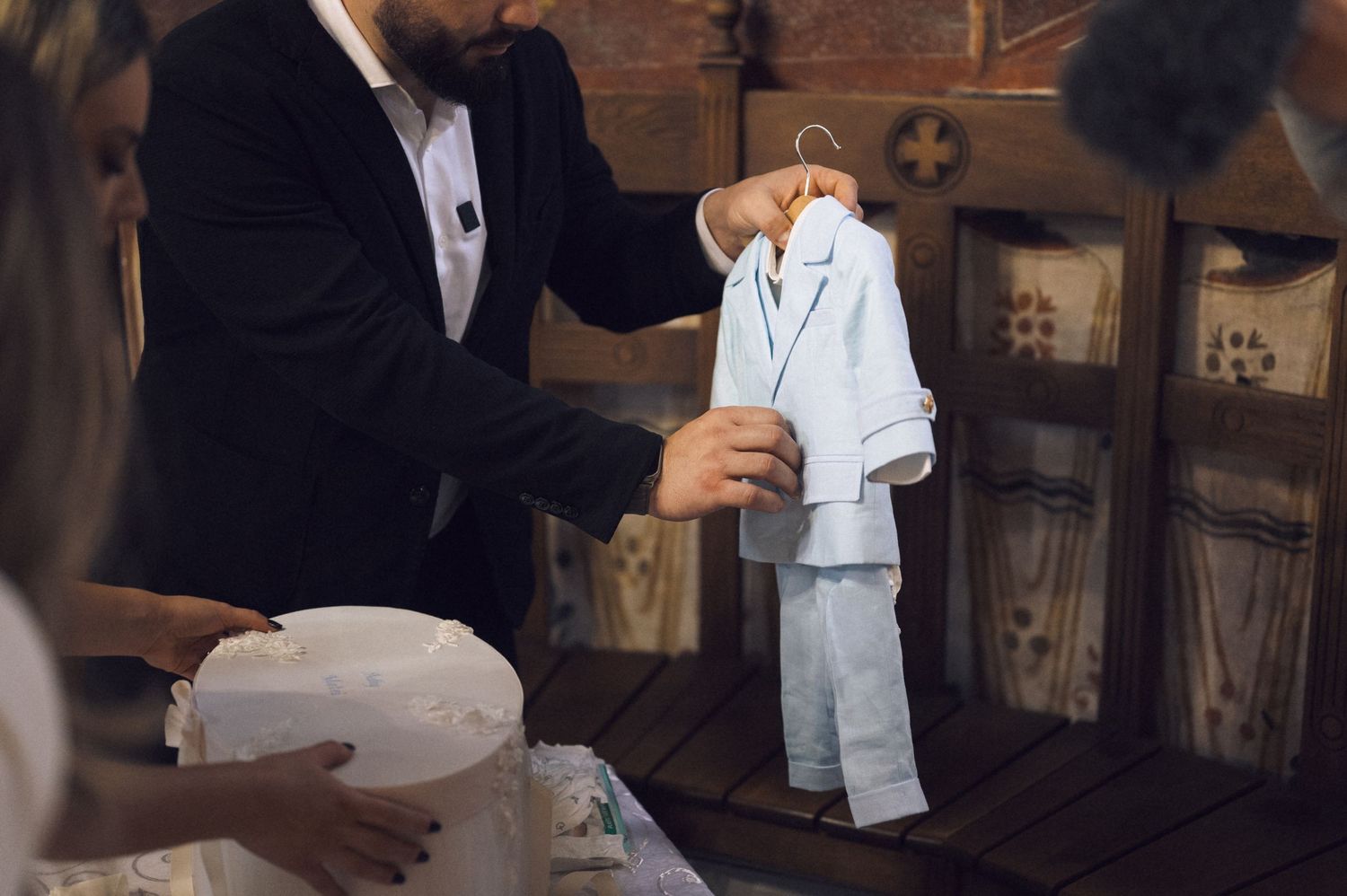 A small white tuxedo suit being displayed on a wooden table next to formal wear.