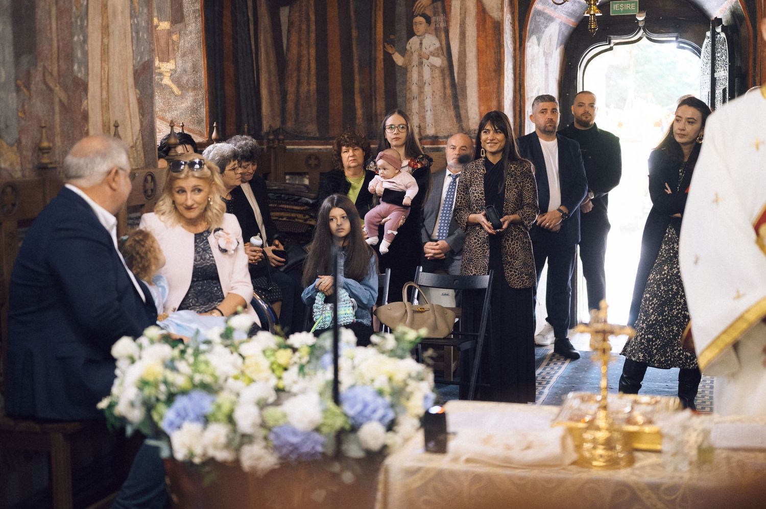 A wedding ceremony takes place in a historic church with floral arrangements and guests gathered around the altar.