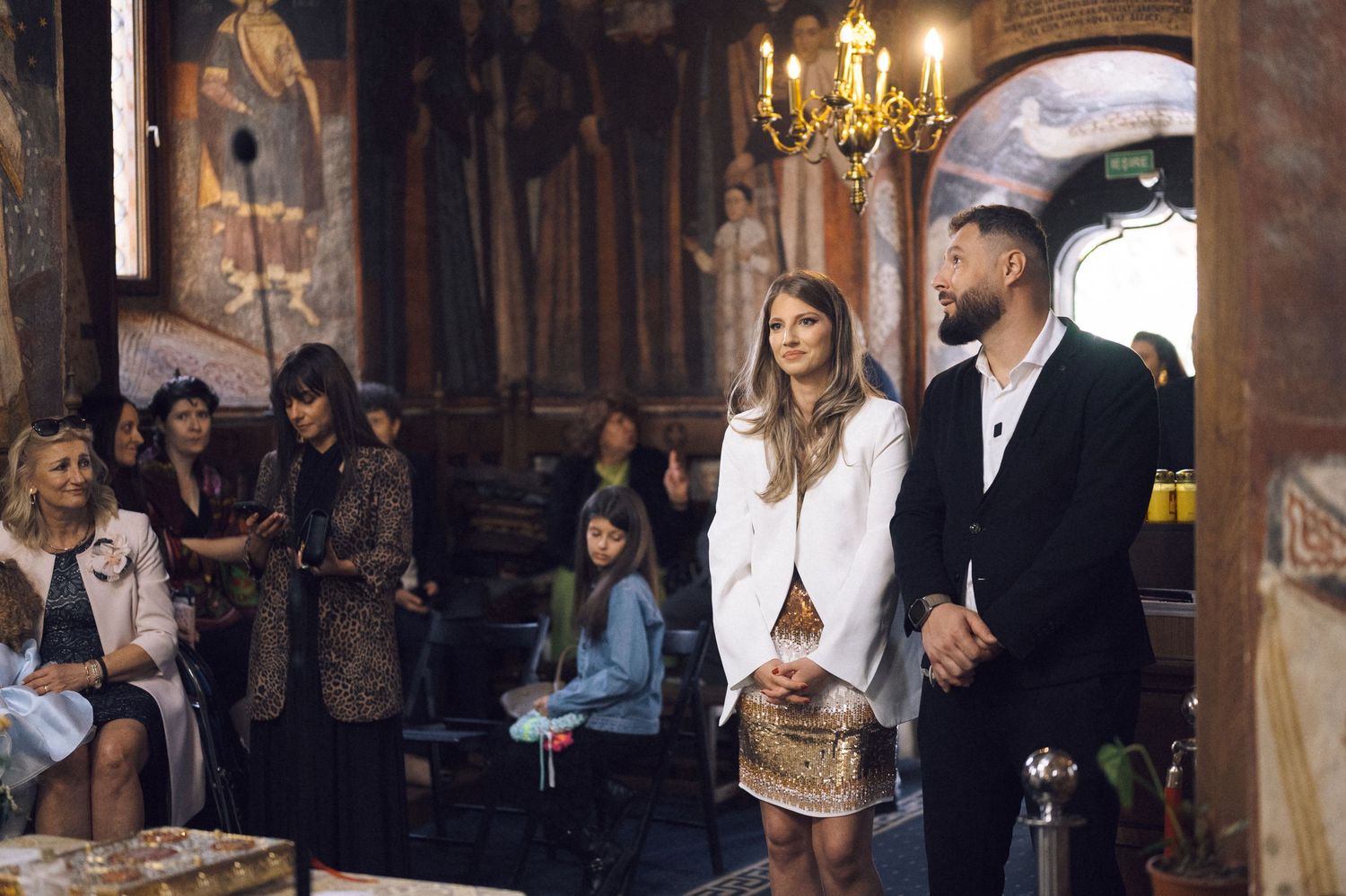 People gather in an elegant room with chandeliers and ornate decor during what appears to be a formal event.