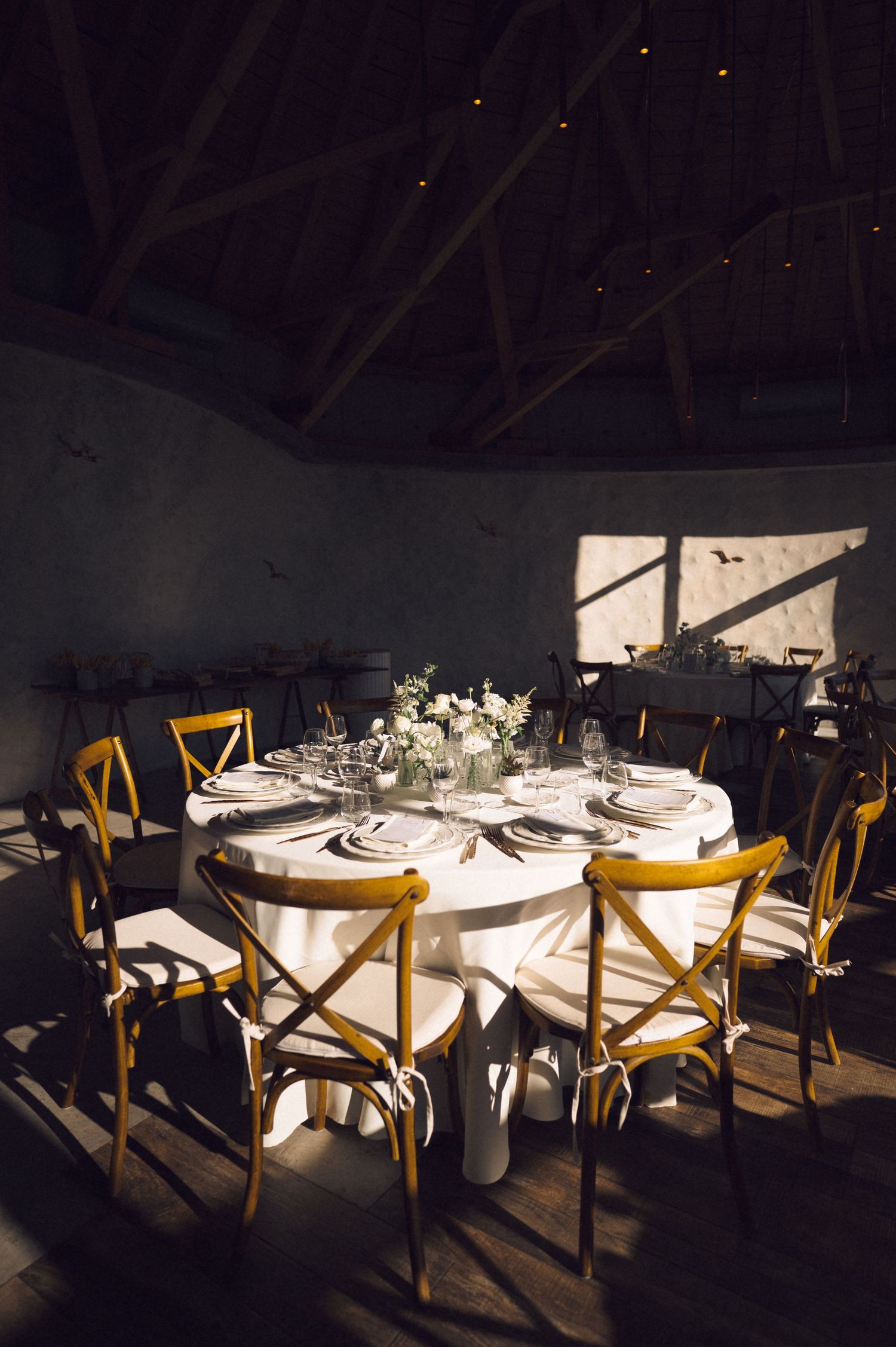 Round dining tables with white tablecloths and yellow chairs arranged in a dimly lit restaurant setting.