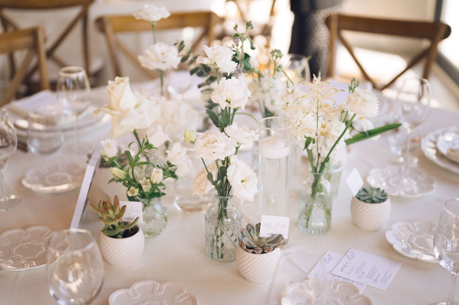 Elegant wedding reception tables set with white linens, delicate floral centerpieces, and crystal glassware.