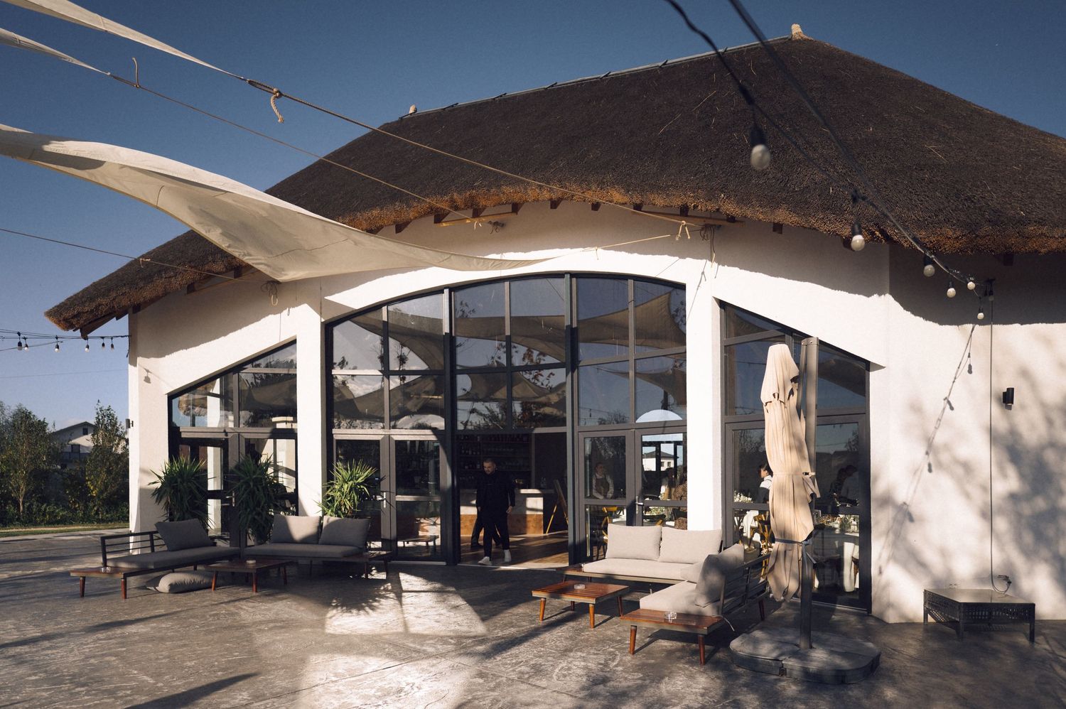 A panoramic view of a modern covered outdoor patio area with white columns and wooden beams against a blue sky.