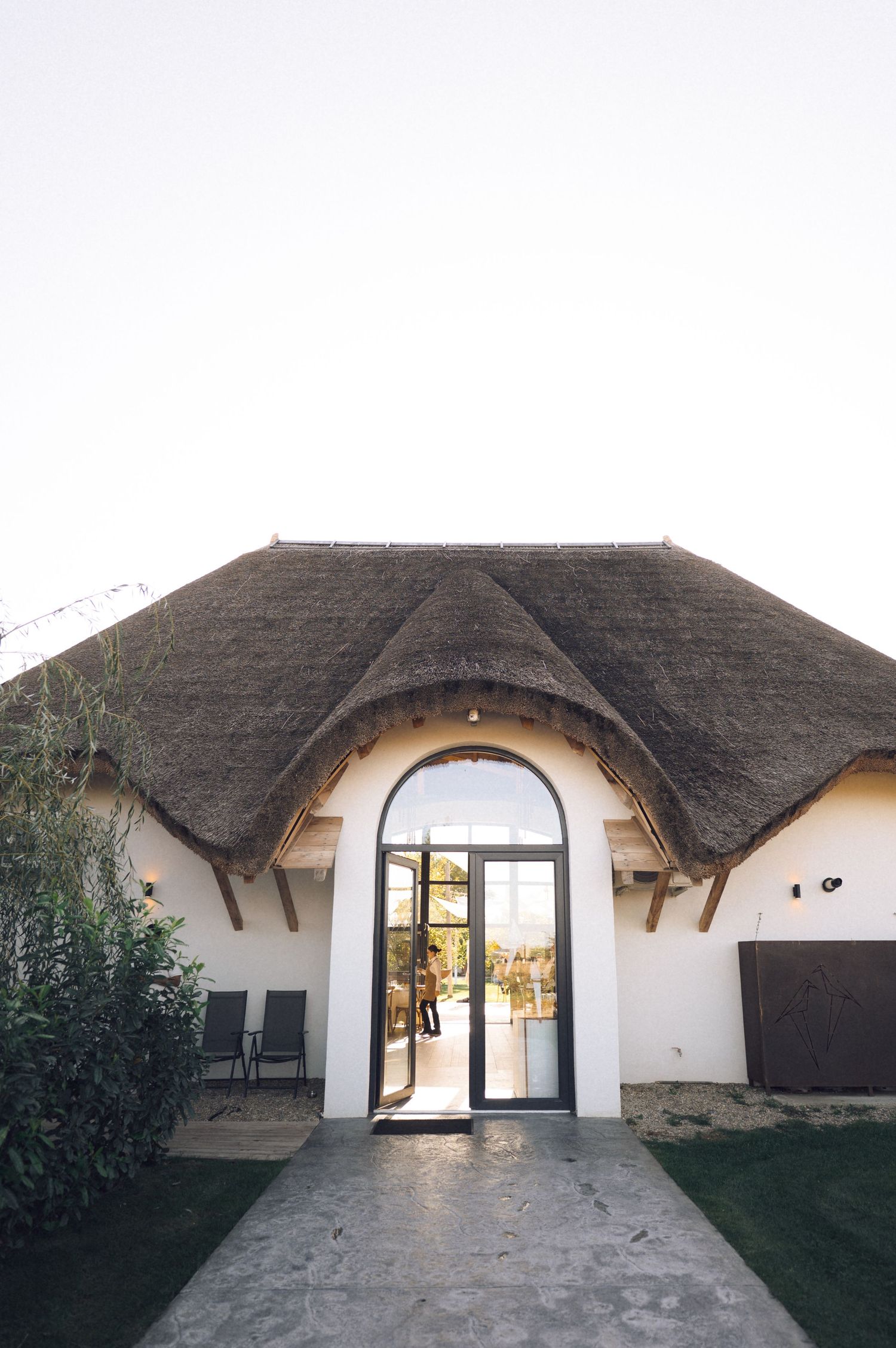Modern curved archway entrance with white walls and thatched roof design showcases contemporary eco-friendly architecture.