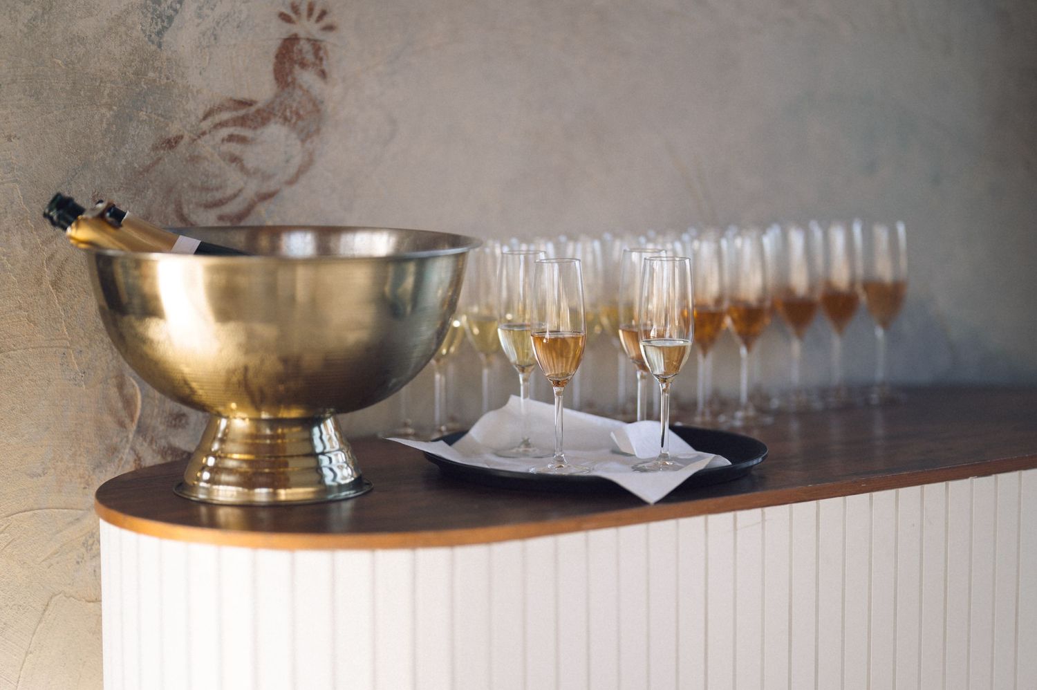 Row of empty wine glasses arranged on wooden bar counter with metallic bowl in background.