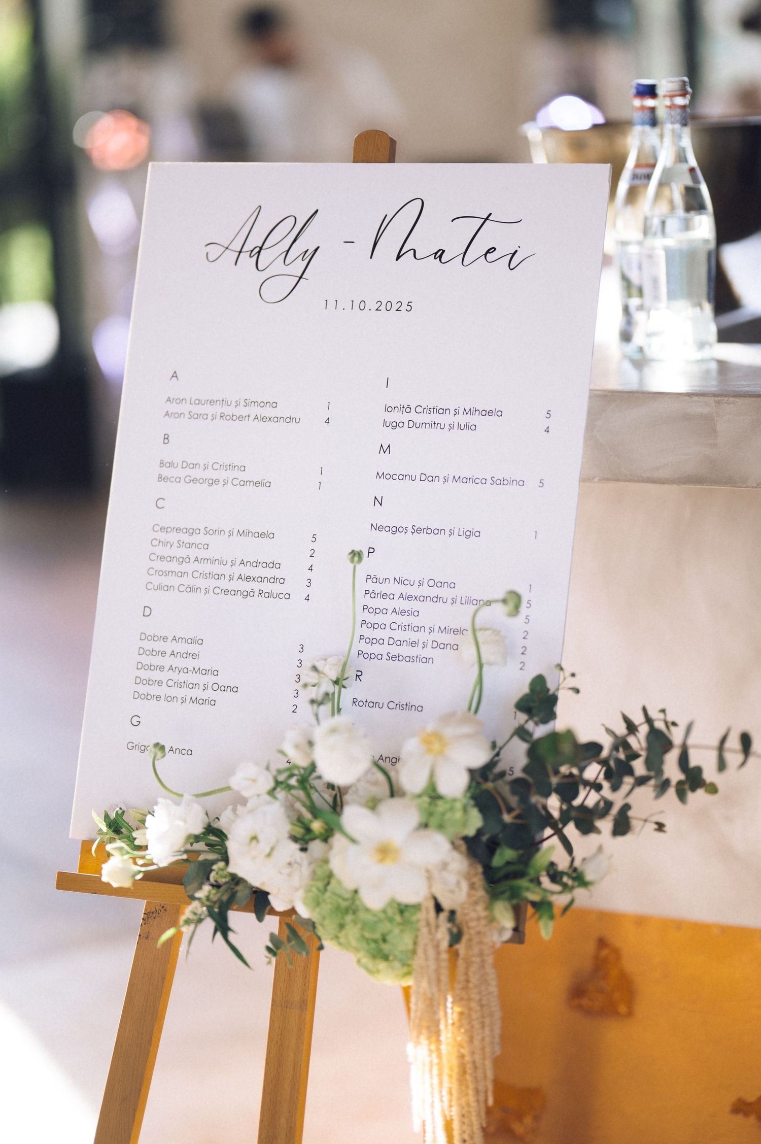 Elegant wedding menu card displayed on gold easel with white floral arrangement and greenery decorations.