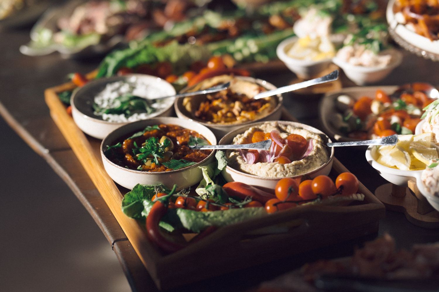 Rustic wooden table set with various dishes of roasted vegetables, sauces, and fresh herbs in cast iron pans.