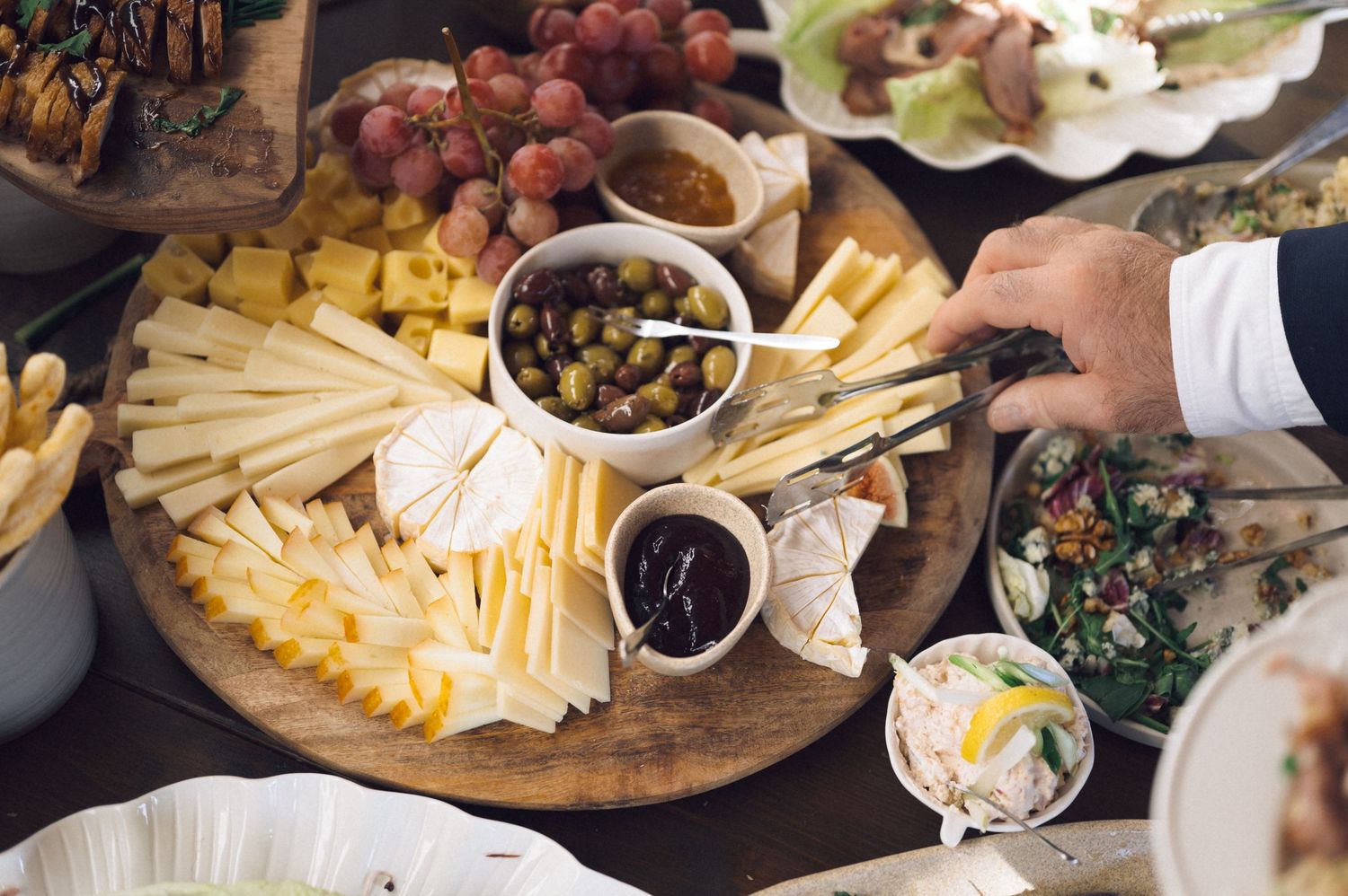 A wooden charcuterie board displays an assortment of cheeses, meats, fruits, and nuts arranged for entertaining.
