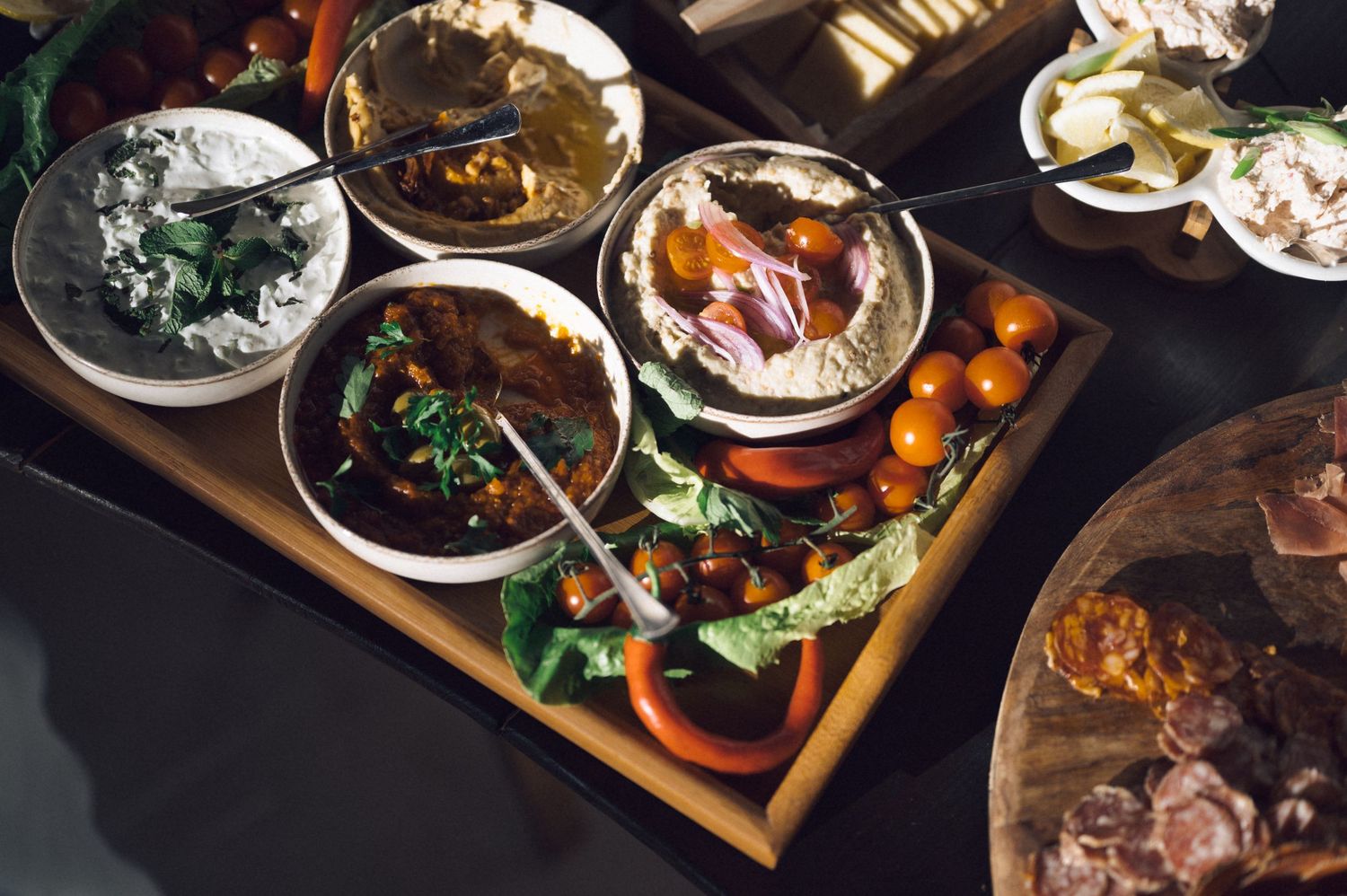 A wooden serving board displays various Asian dishes including dumplings, noodles, and stir-fried vegetables in small bowls.