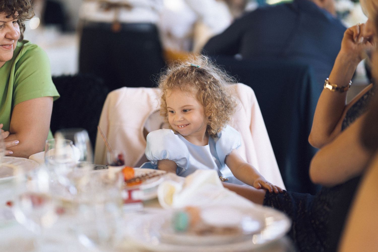 A young guest with curly hair sits at an elegant table setting during a formal dining event.
