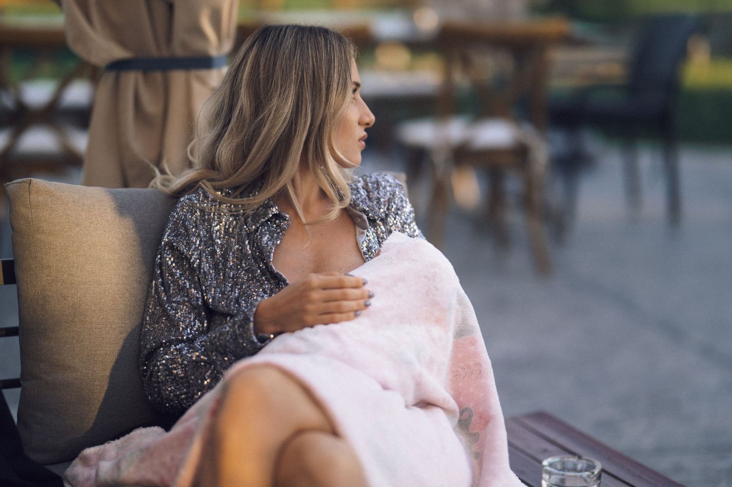 A person in a lace top sits outdoors while holding a pink cotton candy against a blurred background.