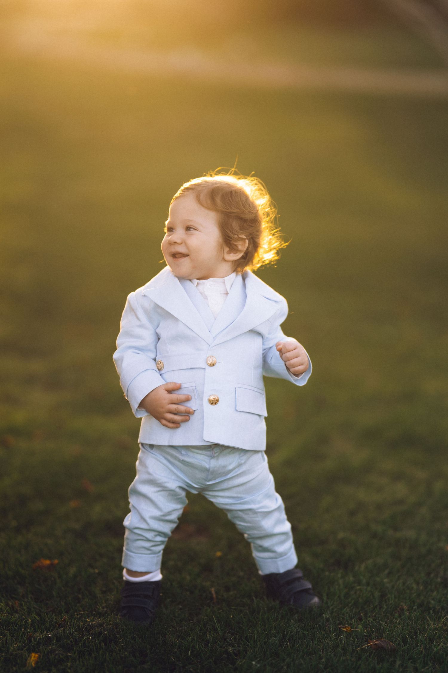 Small child wearing all white clothing plays on grass during golden hour sunset lighting.