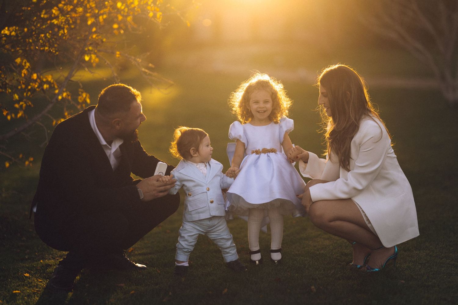 Family members sit together in golden sunlight during an outdoor autumn photo session in a park.