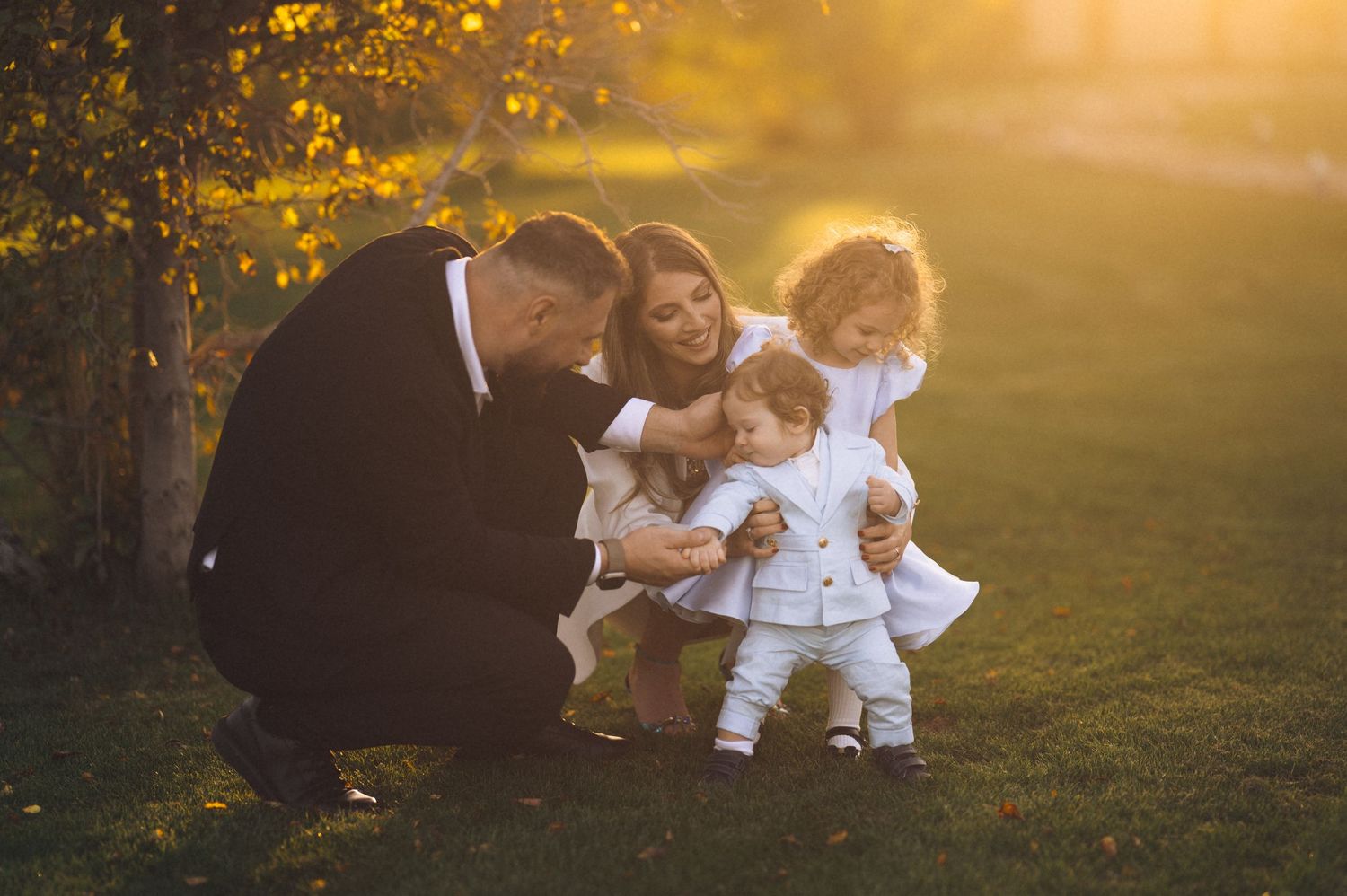 A family sits together in a sunlit meadow during golden hour as autumn leaves fall around them.