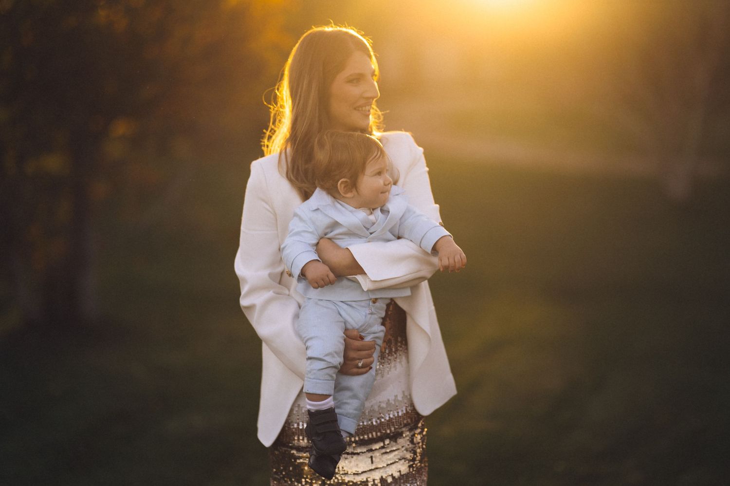 A mother and child share tender moments in a golden sunset field creating an ethereal backlit silhouette.