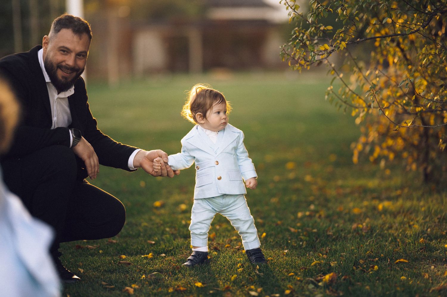 A parent and child play together in a park with autumn leaves and golden sunlight filtering through the trees.