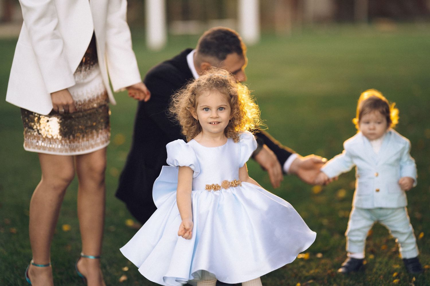 Children in white dresses and blue outfits playing together on a grassy lawn in summer.