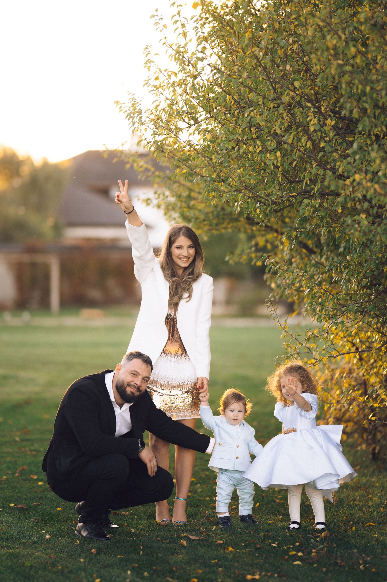 Family poses together outdoors on a sunny autumn day with fall foliage and golden light in background.