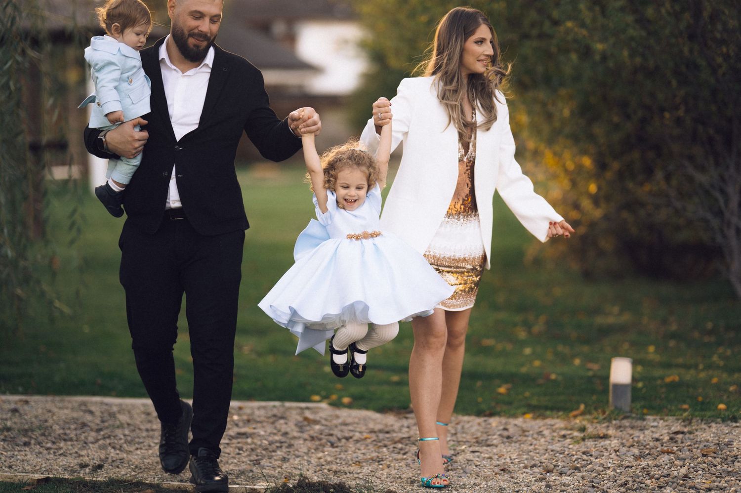 A family in coordinated white and black outfits walks together through a park during an autumn photoshoot.