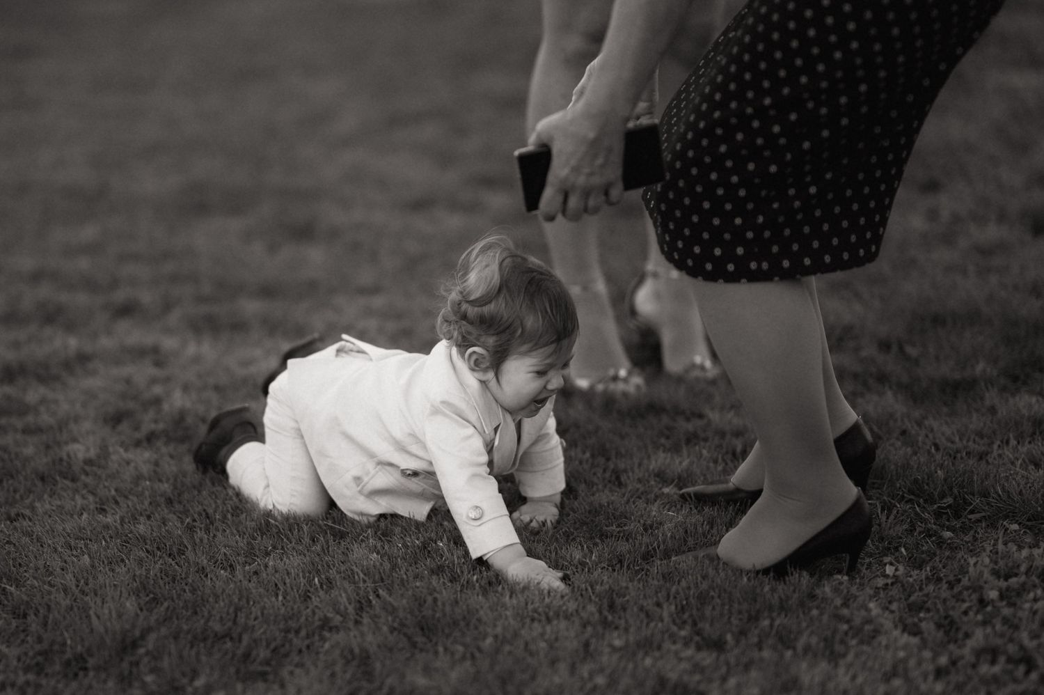 A sequence of black and white photographs showing a baby learning to crawl on grass outdoors.