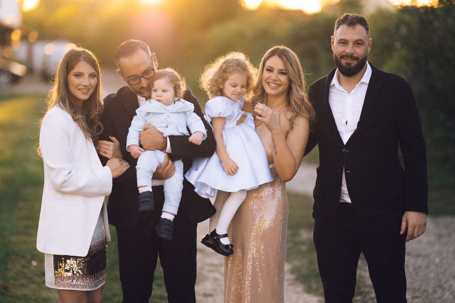 A family wearing coordinated white and beige outfits poses together outdoors during golden hour sunset.