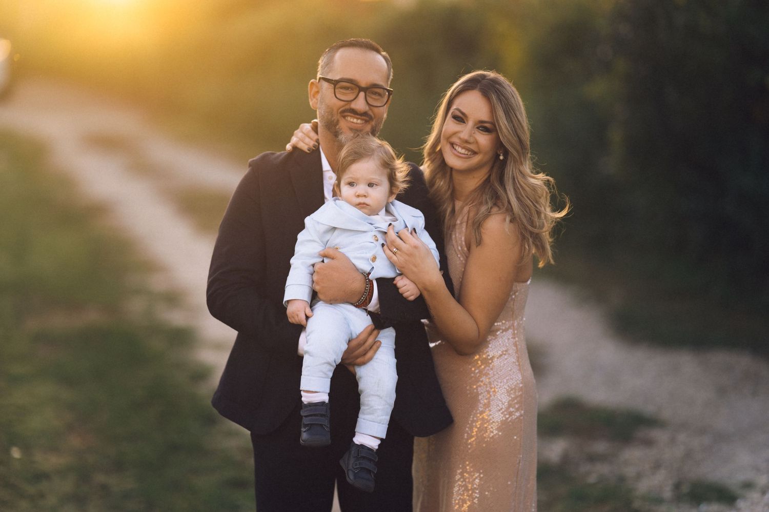 A couple and their baby share tender moments during a sunset photoshoot on a sandy path.