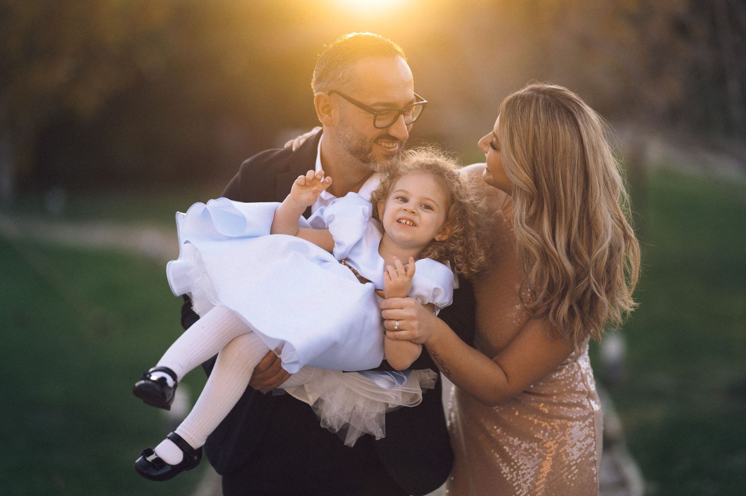 Family embraces outdoors during golden hour sunset with soft glowing light in the background.