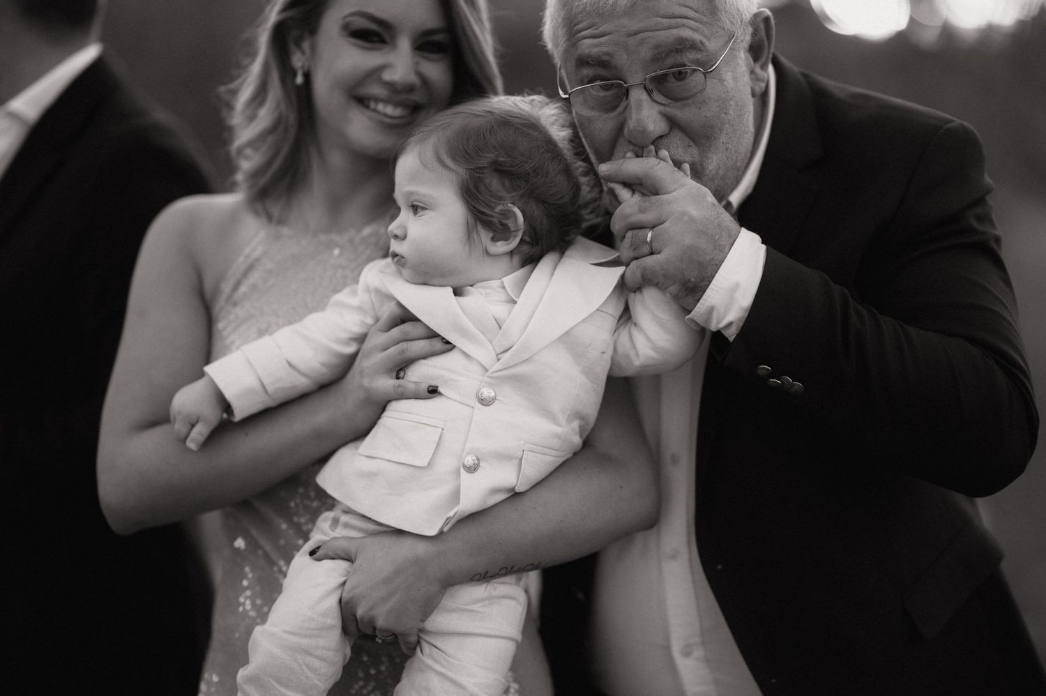 Black and white photo series showing tender family moments between adults and a baby in formal attire.