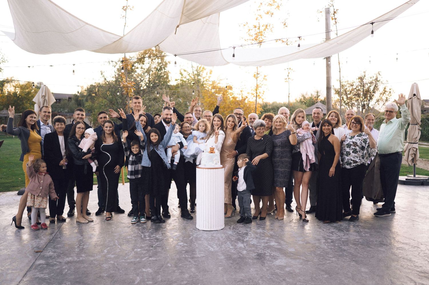 A large wedding party poses together outdoors in formal attire during a sunset celebration.