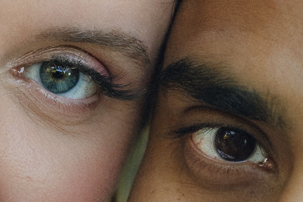 A close-up macro shot of two different colored eyes side by side showing contrasting eye colors and skin tones.